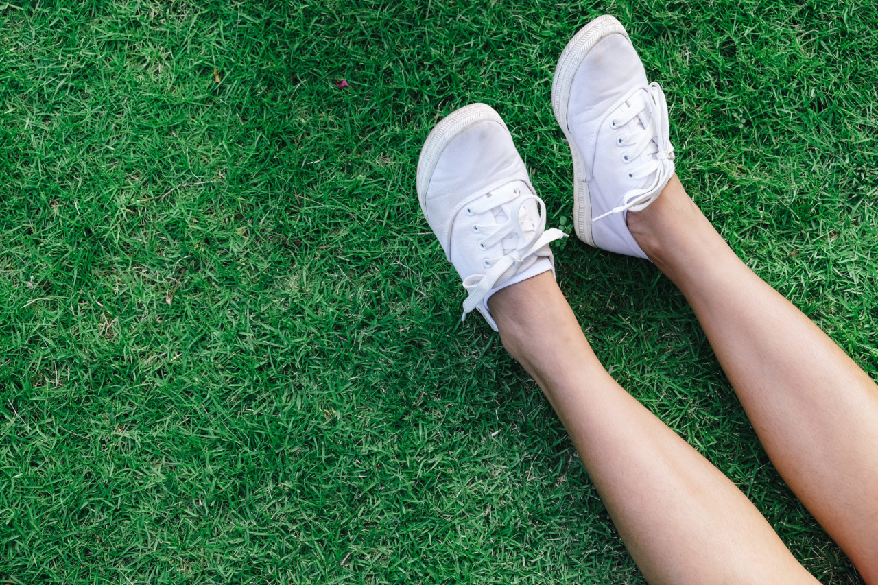 Las piernas de una persona sobre el césped con zapatillas blancas